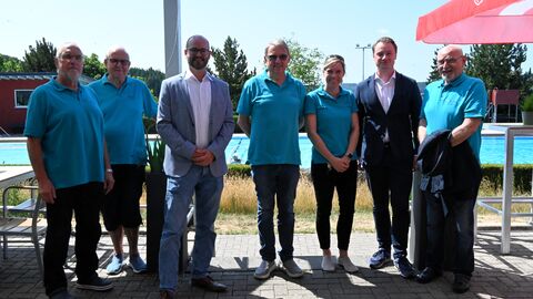 Mehrere Männer stehen vor Becken im Freibad.
