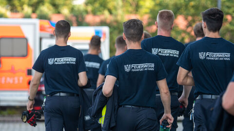 Mehrere Personen mit Shirts mit der Aufschrift "Feuerwehr Frankfurt am Main" laufen über ein Gelände.