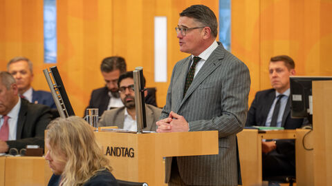 Mann im Anzug hält Rede an Rednerpult.