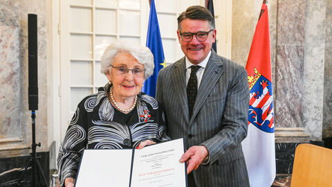 Eine Frau und ein Mann stehen nebeneinander und halten eine Urkunde hoch.