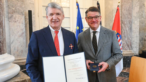 Zwei Männer stehen nebeneinander und halten eine Urkunde hoch.