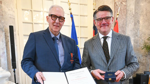 Zwei Männer stehen nebeneinander und halten eine Urkunde hoch.