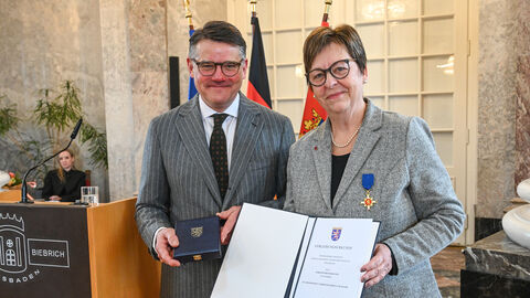 Eine Frau und ein Mann stehen nebeneinander und halten eine Urkunde hoch.