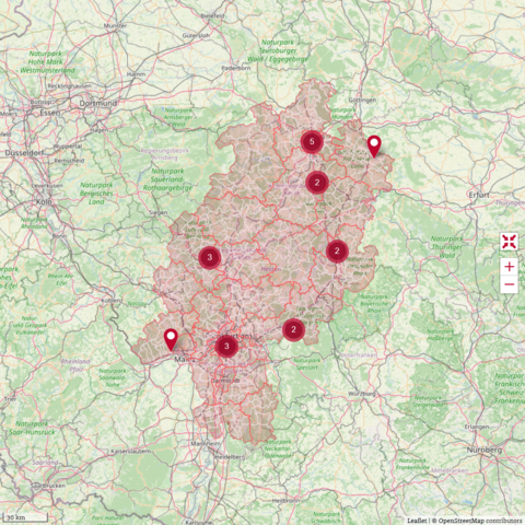 Es ist eine rot unterlegte Landkarte des Bundeslandes Hessen zu sehen, auf der einige dunkelrote Stecknadeln markiert sind.